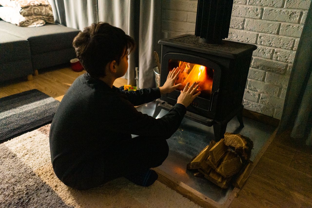 services-01 A child warms hands by a wood stove in a cozy living room, creating a warm winter ambiance.