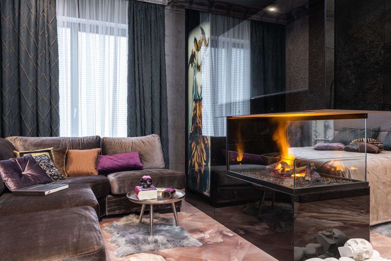 who-we-are Interior of modern apartment with comfortable couch and side table with decorations placed near burning fireplace at bed in stylish room