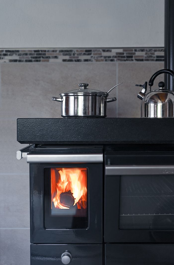 why-choose-me Modern kitchen featuring a classic wood stove with a metal pot and kettle, blending contemporary and traditional styles.
