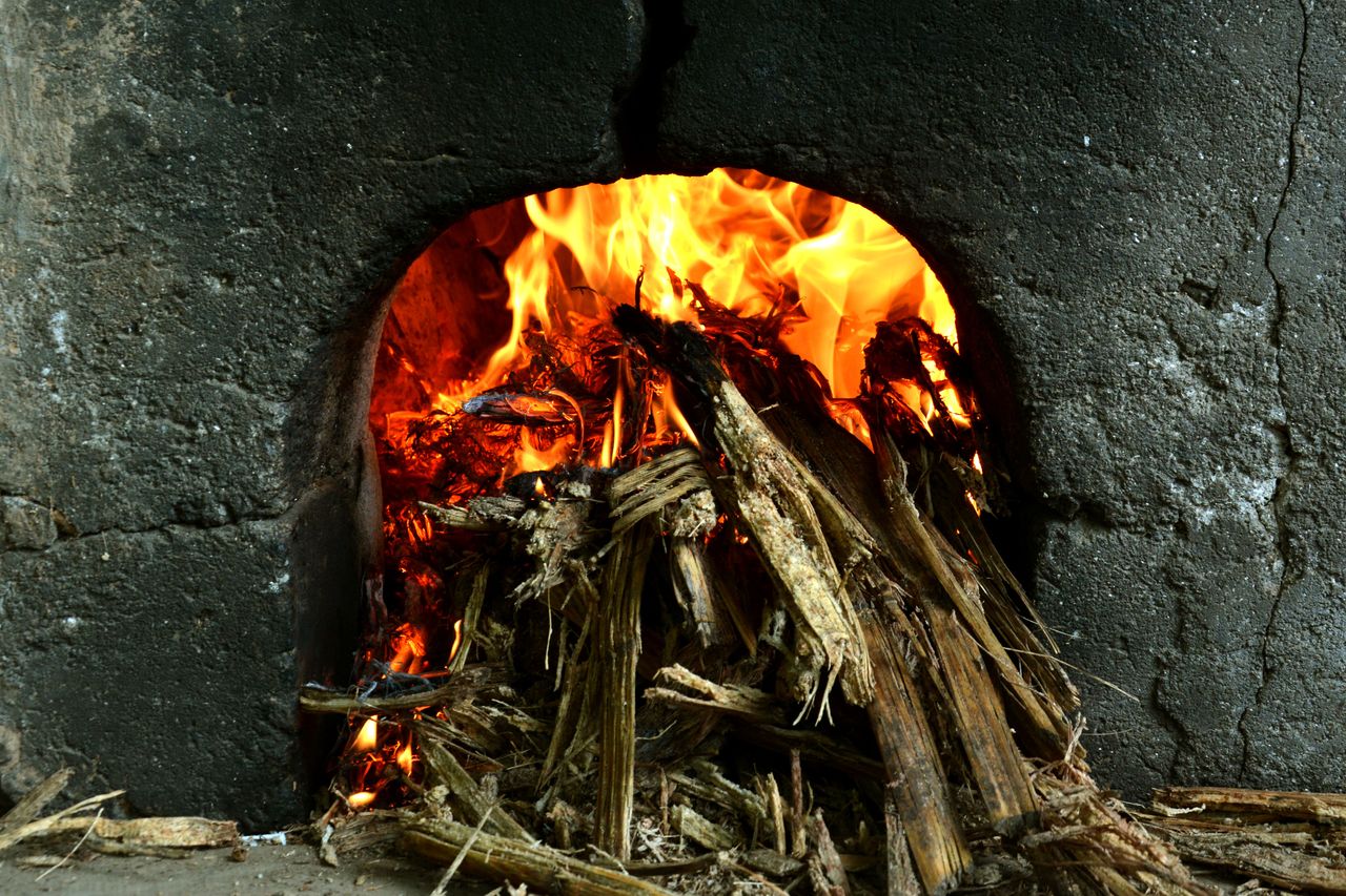 my-steps Close-up of a rustic wood-fired clay oven with burning wood and vibrant flames.